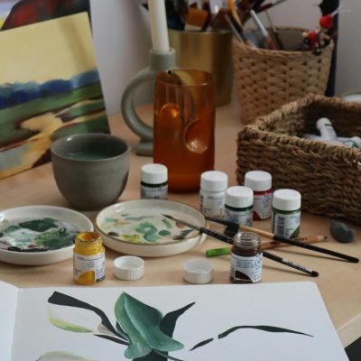 Artistic setup with painting supplies and canvas featuring a botanical illustration.